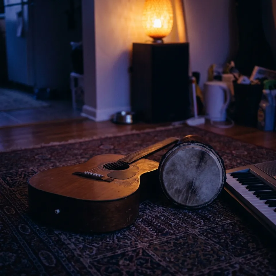 Une guitare, un petit tambour et le bord d'un clavier posés sur un tapis.